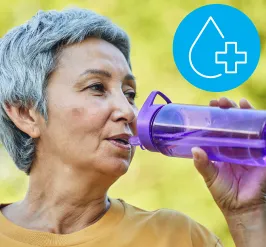 An older woman taking a sip from her purple water bottle. A water droplet with a plus symbol on it is in the upper right corner. 