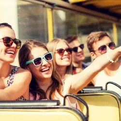 a group of teens on a bus smiling and pointing to something interesting outside the window.