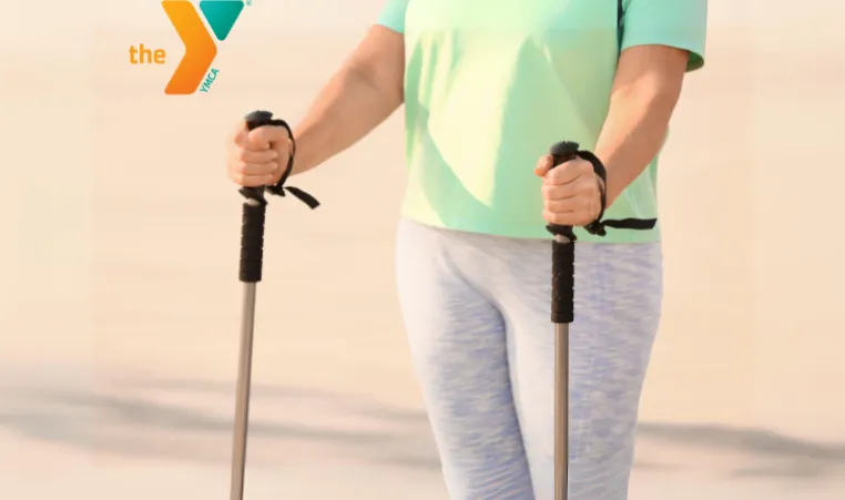 A close up shot of a woman in work out leggings with a walking pole in each hand.