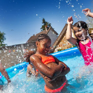 A group of young children splashing around in a backyard pool. 