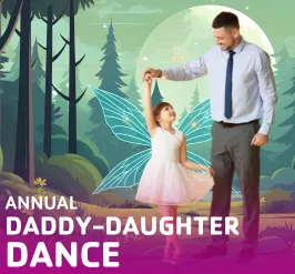 A little girl in a dress and fairy wings dancing with her dad.
