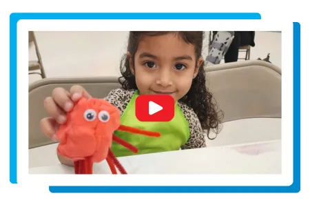 a little girl with her art project. A video play button.
