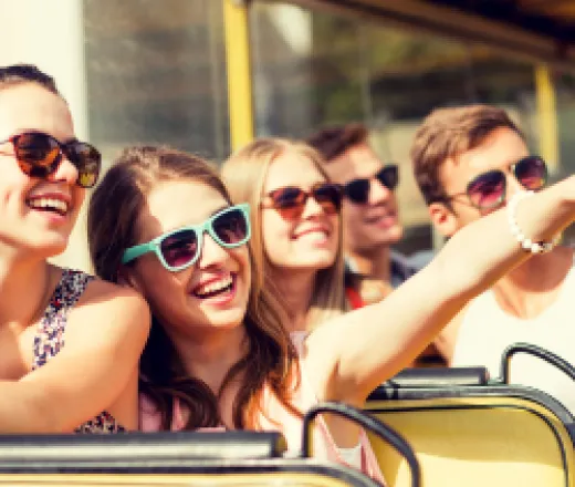 a group of teens on a bus smiling and pointing to something interesting outside the window.