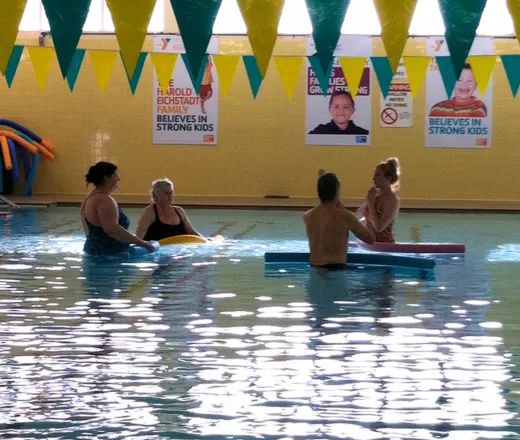 A small group of women and men follow along with a water fitness instructor in the 20th ave pool.