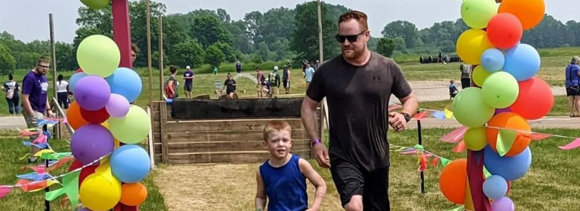 a father and son running through a balloon covered finish line at the annual mud run.