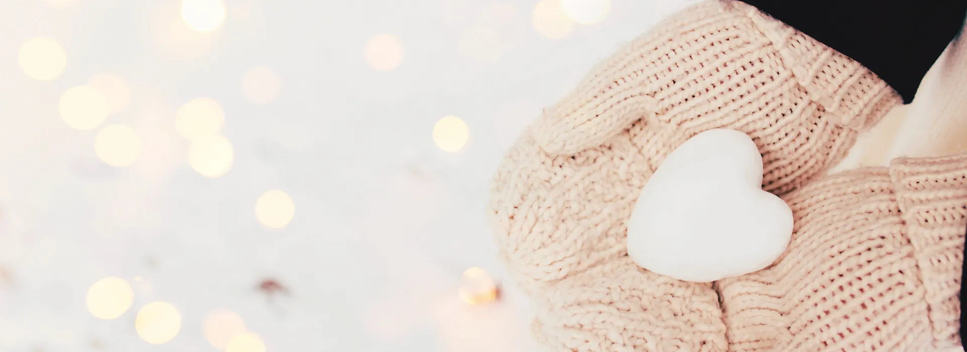 a person's hands in white mittens holding a snowball shaped like a heart