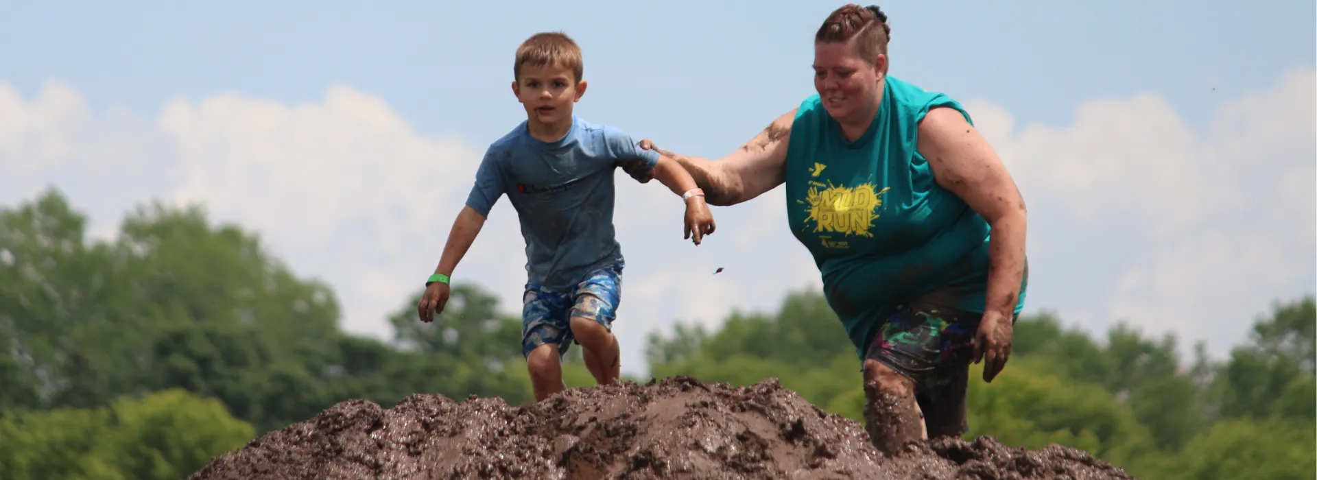 A very muddy volunteer helping a child climb over a mud pile at the kids mud run.